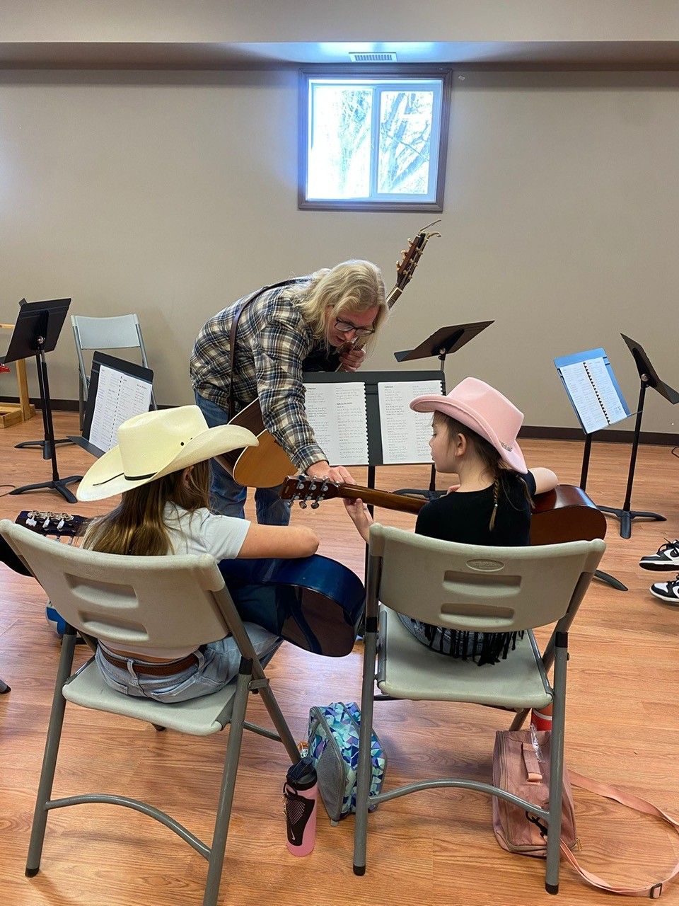 Instructor helping two guitar players in cowboy hats with a chord.